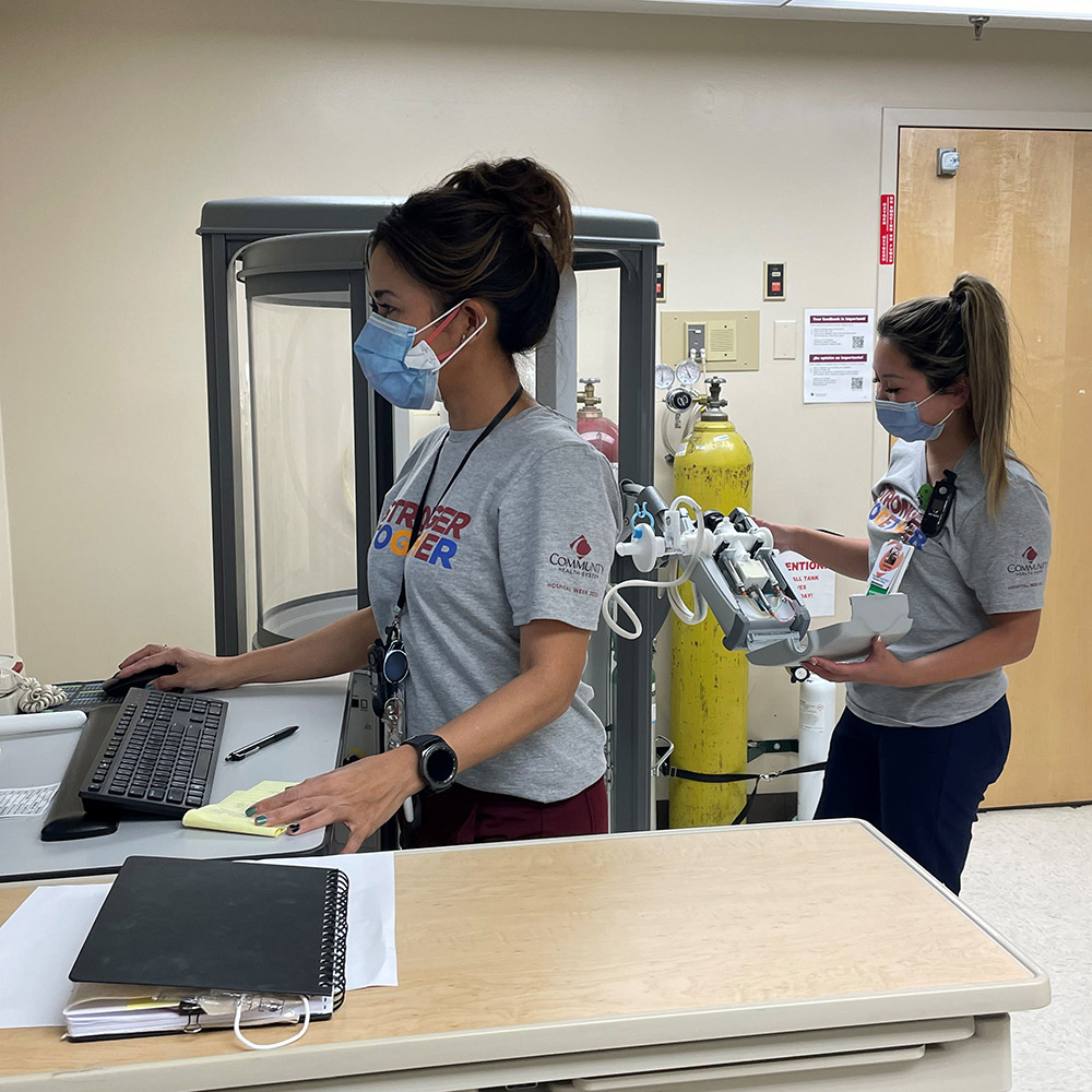 Two female respiratory therapists in masks monitor lung measuring equipment