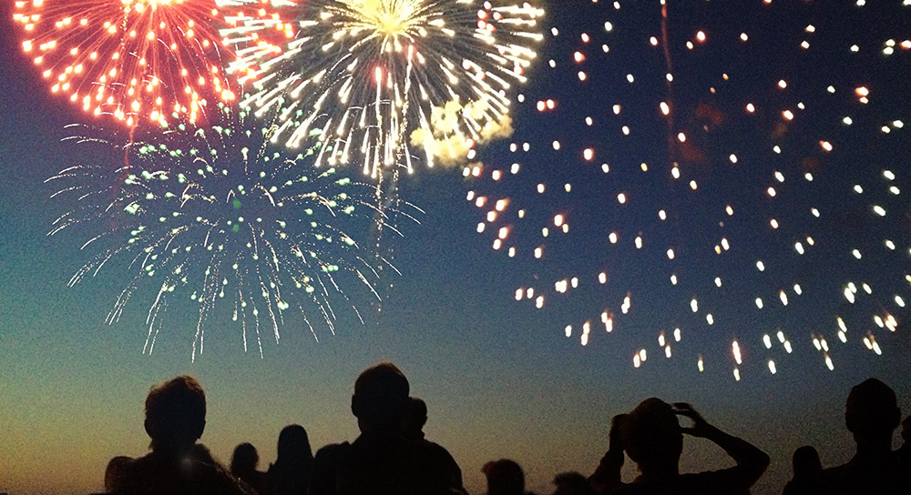 Silhouetted figures watch overhead fireworks