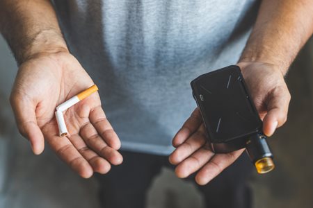 person holding a broken cigarette in one hand and a vape device in the other