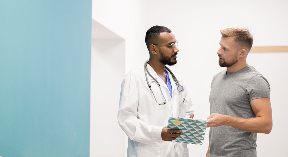 A male doctor and a male patient confer in a hospital hallway