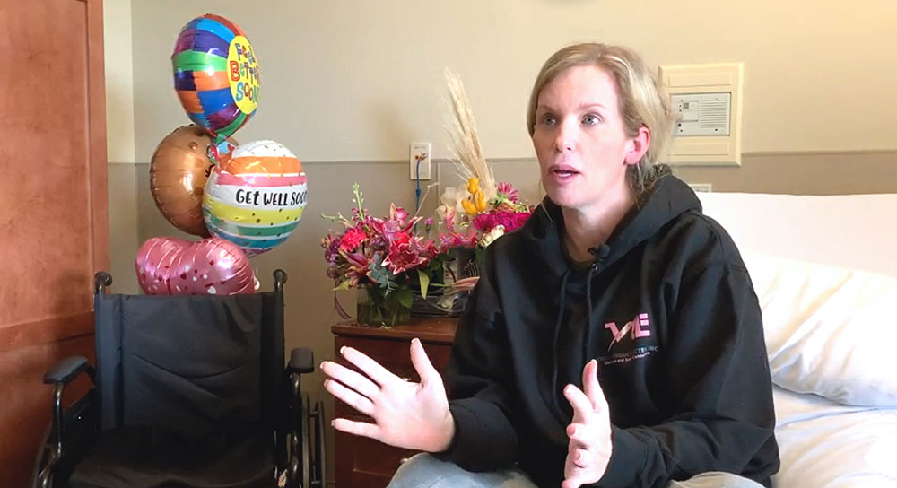 A new mom sits in a hospital bed surrounded by balloons and flowers
