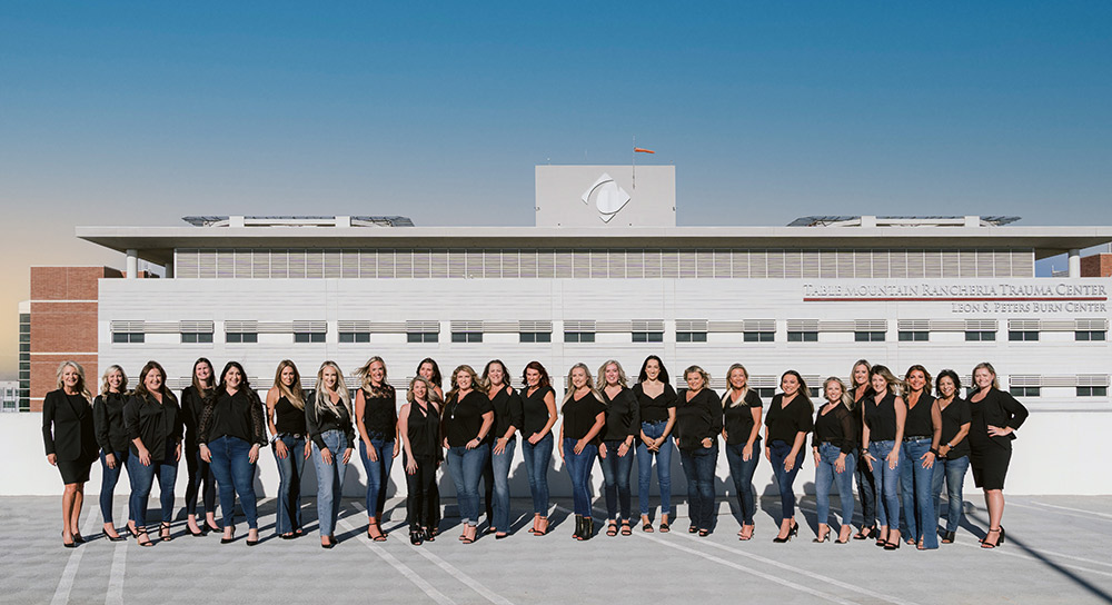 A group of about two dozen women stand in a line near a Community Health System building