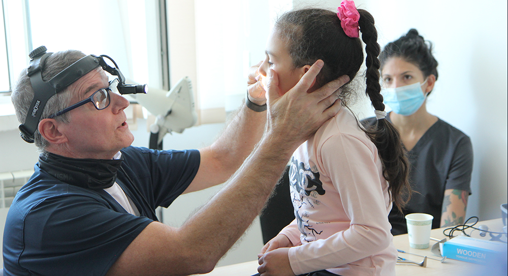 A male doctor examines a young girl as her mother looks on