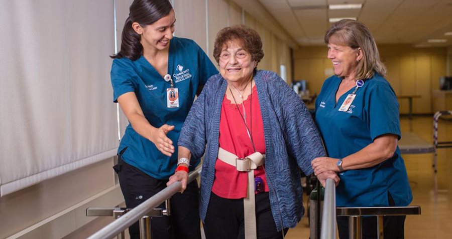 A woman is assisted on a walking pad by two rehab assistants