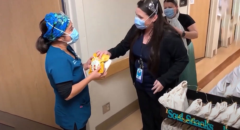 Masked chaplain hands snacks to a masked healthcare worker