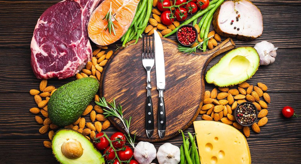 Knife and fork surrounded by various meats, vegetables and cheese