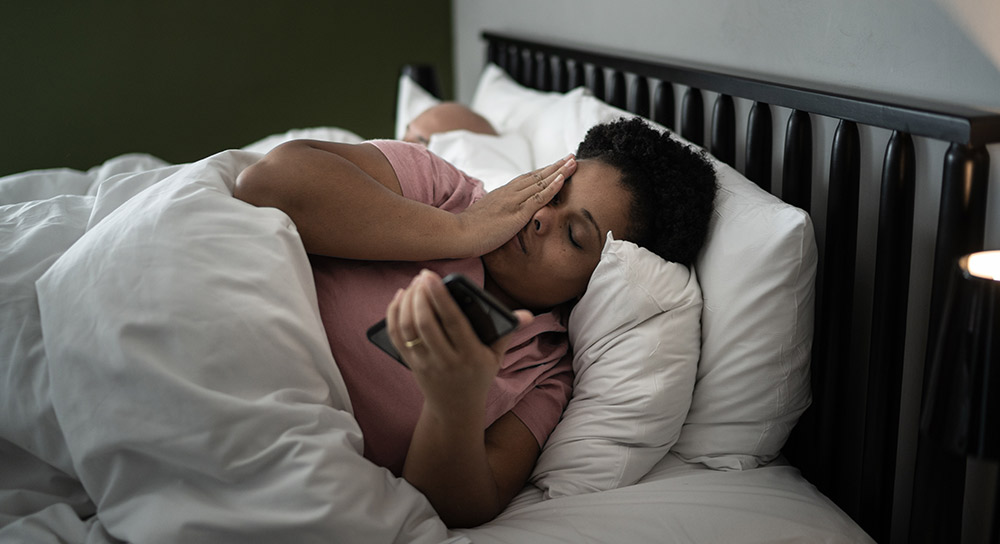 women laying in bed holding her phone and rubbing her face