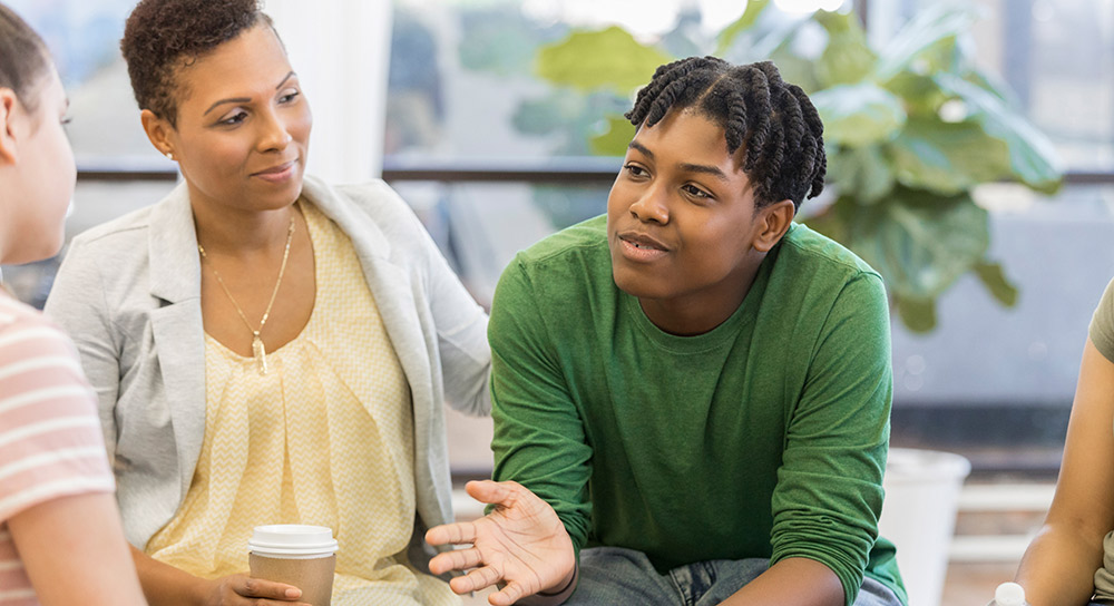 A mother pats the back of a teen boy who is talking
