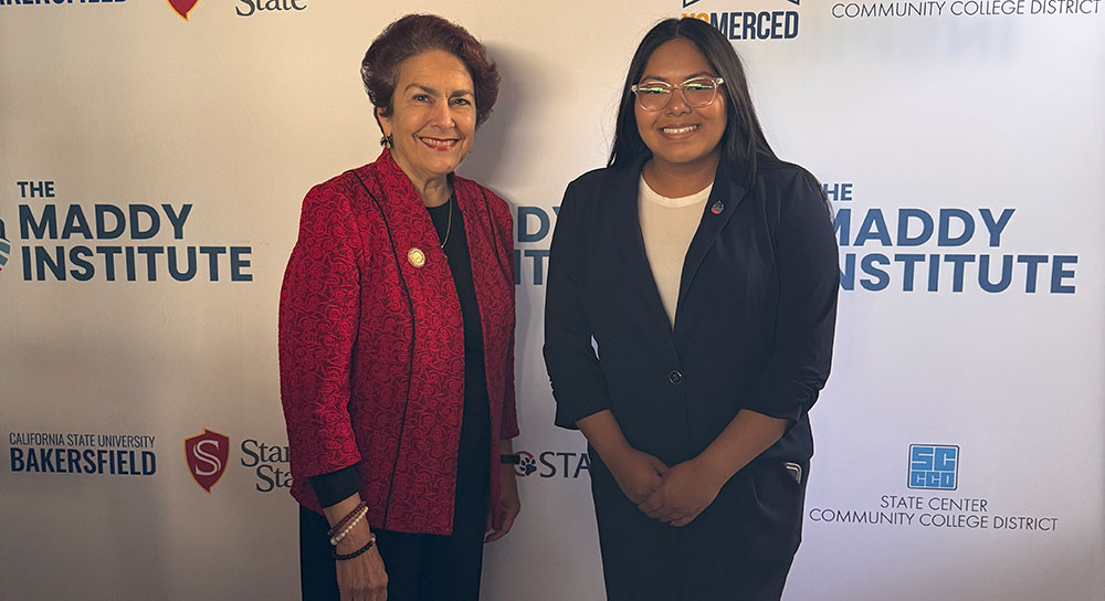 Two women stand in front of a screen with "The Maddy Institute" logo on it.