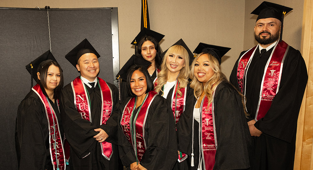Seven college graduates in caps and gowns smile at the camera