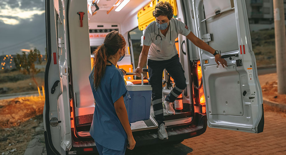 A person in a van leans down to hand a cooler to a healthcare worker on the ground