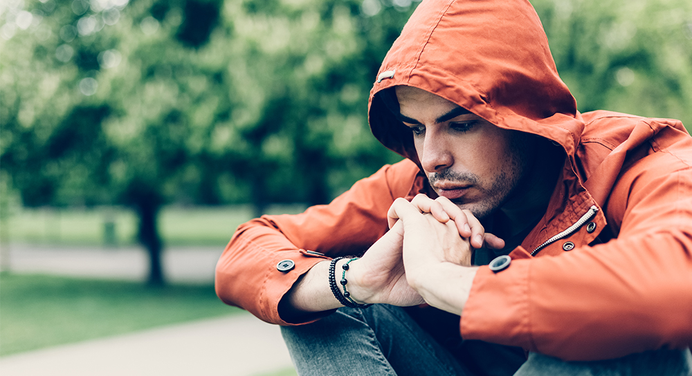 A young man in a hoodie sits in a park