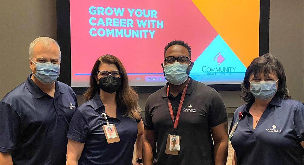Four healthcare workers in masks pose in front of a screen