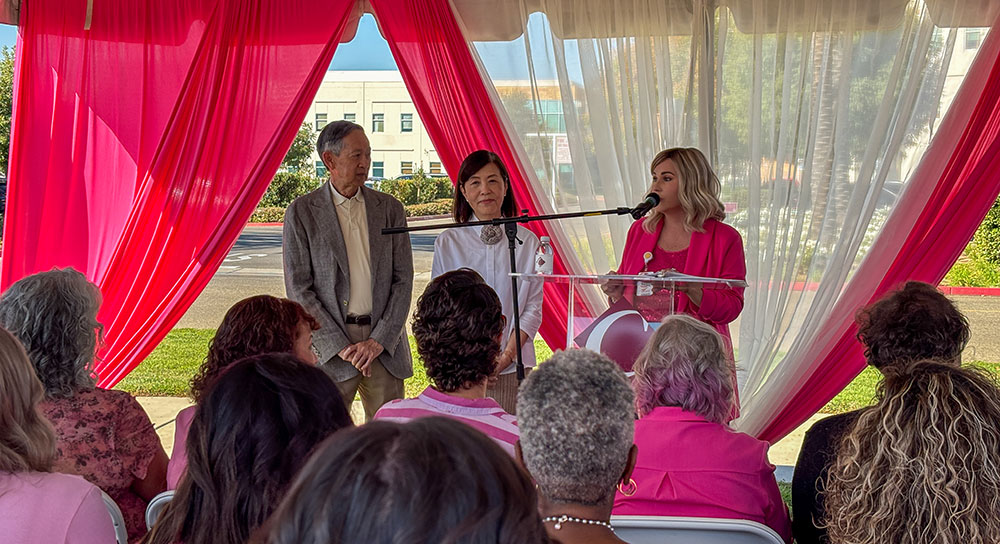 A crowd watches a presentation to two donor under a pink tent