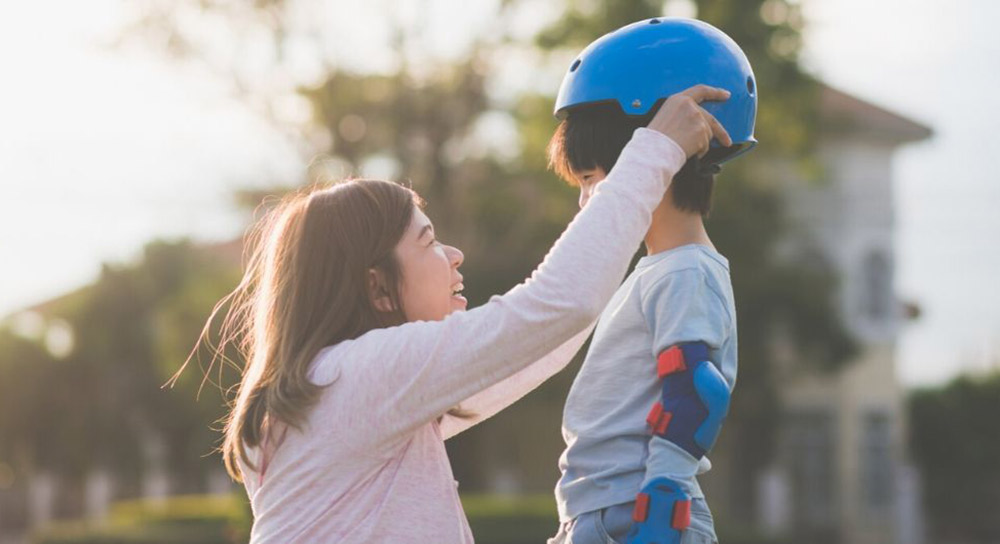 mom puts a helmet on her young son