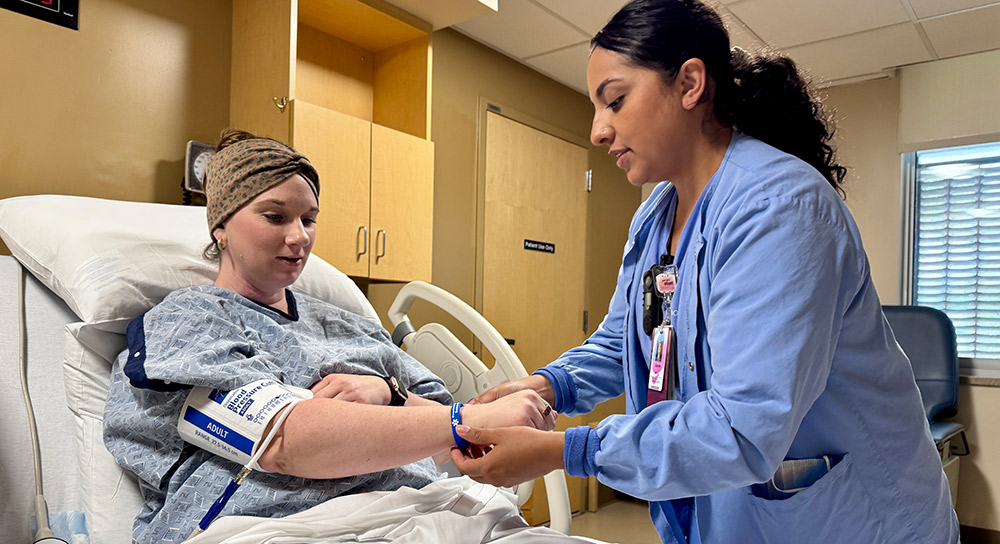 A healthcare worker puts a blue wristband on the arm of a pregnant person in a hospital bed