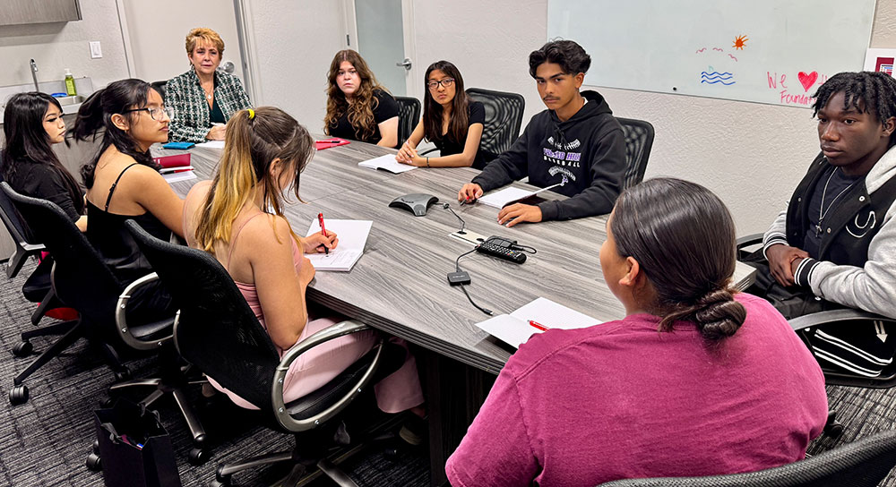 Eight high school kids and a teacher sit around a conference table
