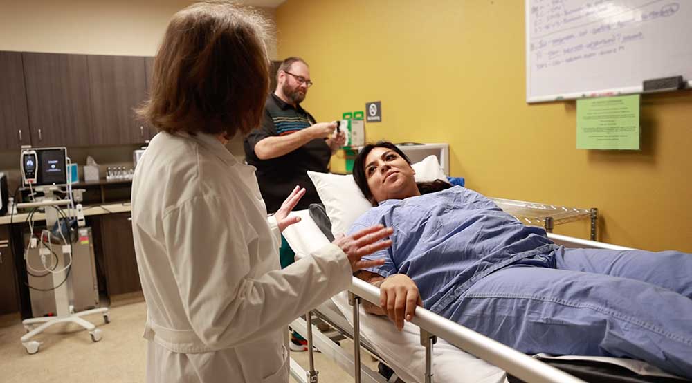 Una paciente en una cama de hospital mira a su médica, que la está preparando para el tratamiento con oxígeno hiperbárico.