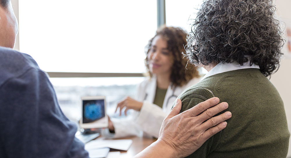 Close up of a patient putting his hand on his wife's shoulder as a doctor explains a procedure