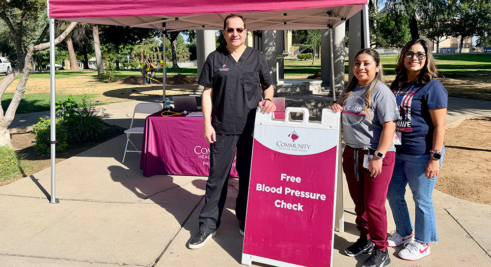 Healthcare workers stand next to a sandwich board that reads, "Free Blood Pressure Check"