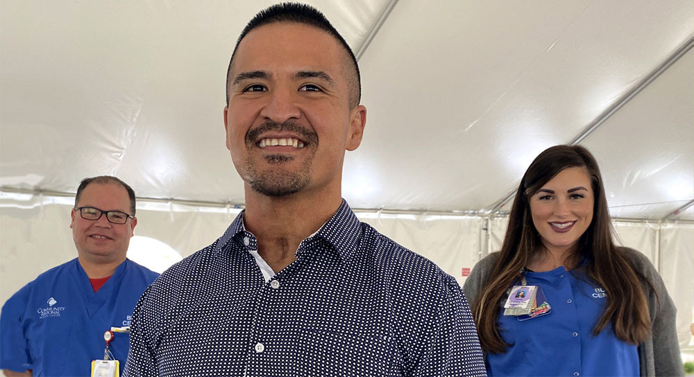 Two healthcare workers, a man and a woman, stand behind a smiling male patient.