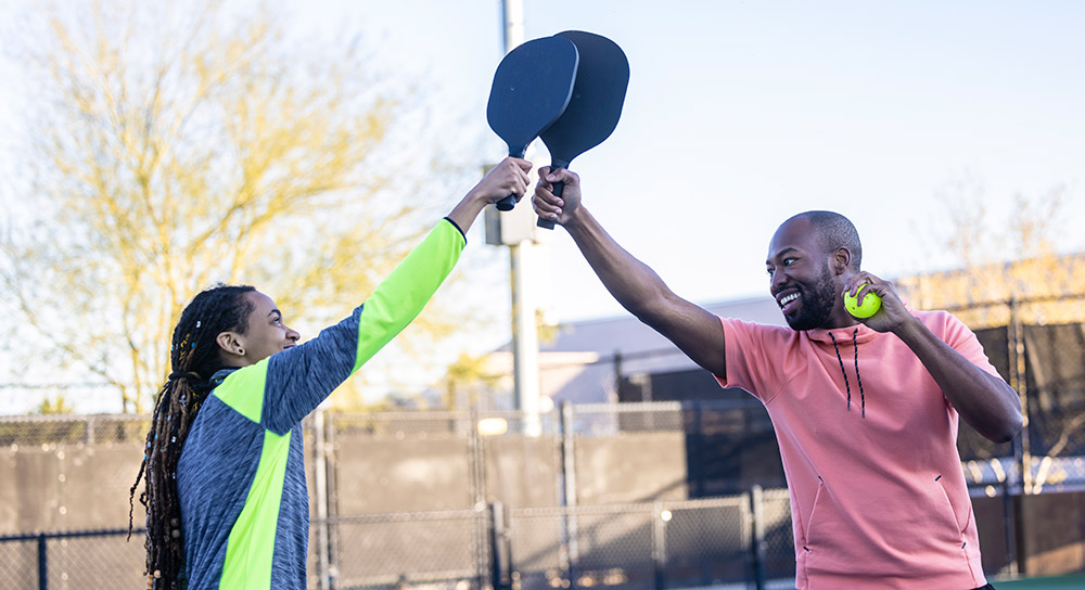 A man and a woman high five with paddles over a pickleball net