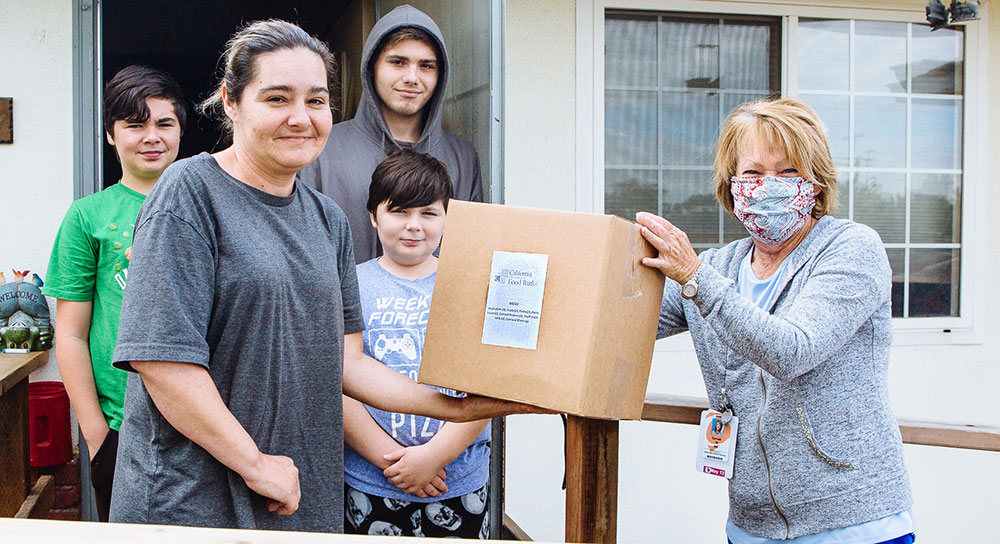 A family receives a box of food from a woman wearing a mask