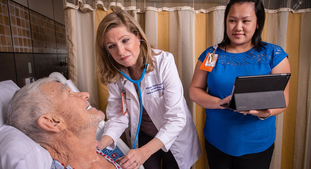 A man in a hospital bed smiles up at two female healthcare workers