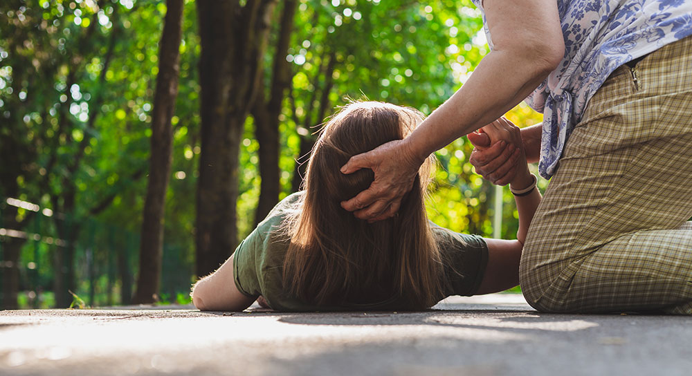 A young woman lies on a sidewalk. Someone is holding her head up and holding her hand