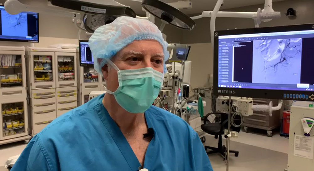 A male masked doctor in mask and scrubs stands in operating room