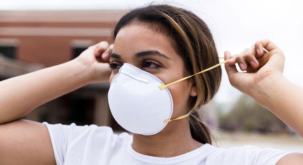 A young Latina woman demonstrates how to wear an N95 mask