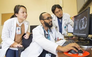 three doctors examine an x-ray on a computer screen