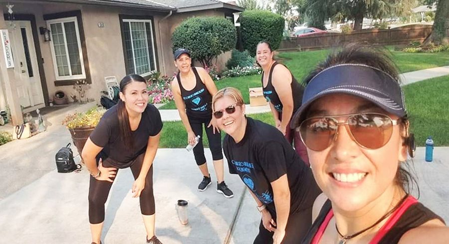 Five women in fitness gear strike a pose with their hands on their knees outside a house