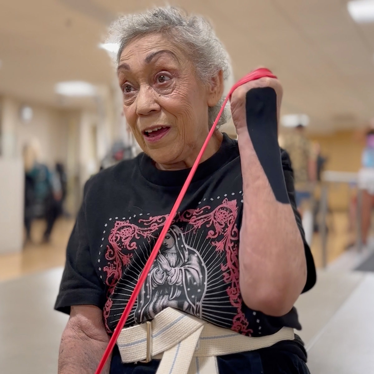 An older Latina woman uses a band to stretch her arms