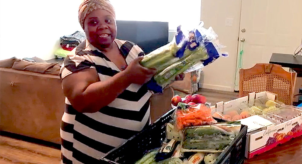 LaToya Rowe stands in a living room and pulls produce from a box