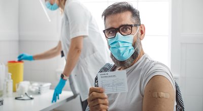 Man in a mask holds up vaccination card