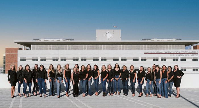 The two dozen or so Founders Club members stand in a straight horizontal line outside and in front of Community Regional Medical Center's Trauma Center with the blue sky above them.