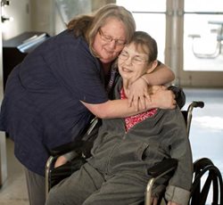 Una cuidadora y paciente en silla de ruedas se abrazan.