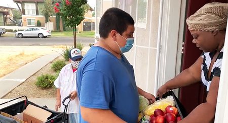 A young man in a mask delivers produce to Latoya Rowe