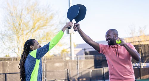 Man and a woman high five with paddles over the net of a pickleball court