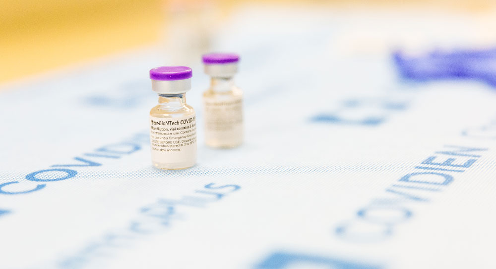 Close up of two vials of COVID-19 vaccine sit on a table.