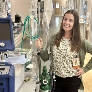 Catrina Cullen smiles in a hospital hallway as she stands next to a mobile IV unit