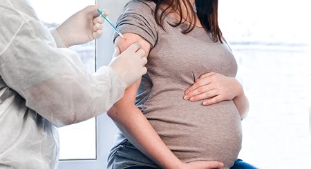 a pregnant woman holds her belly while a doctor administers a vaccine in her arm