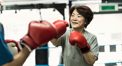 an older Asian woman with red boxing gloves smiles