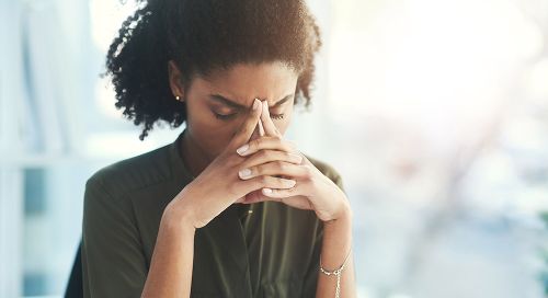 A young Black woman holds her head in her hands.
