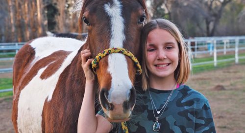 10-year-old Ashlyn Ainger stands smiling next to her horse