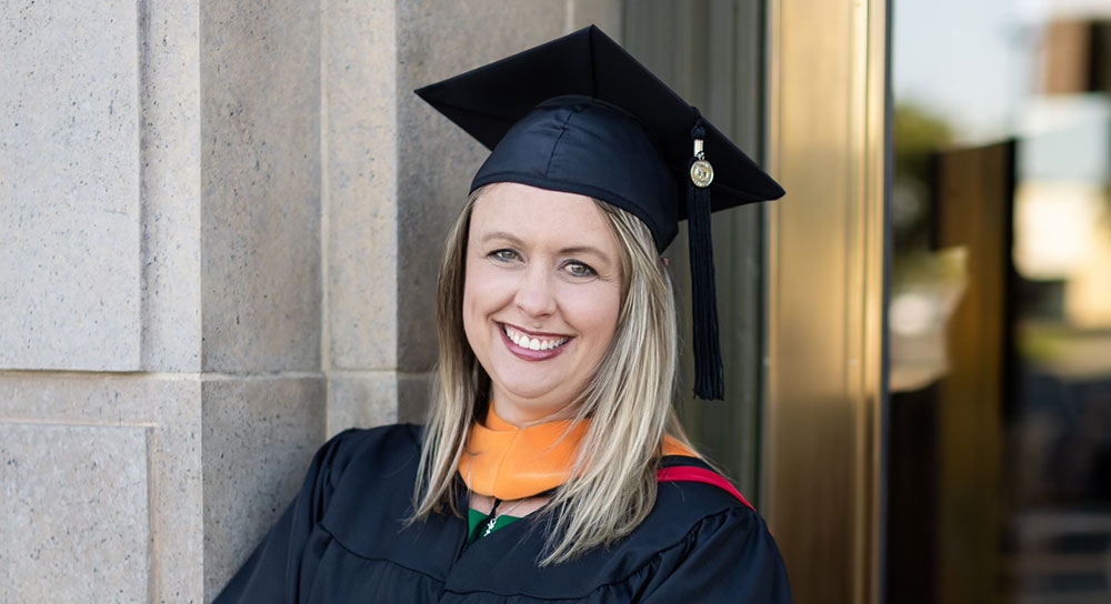 Jenny Guire stands in a doorway with her black graduating cap and gown on.