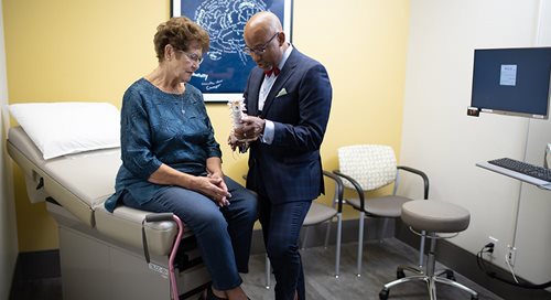 Sentada en la camilla de una sala de examinación, Bonnie "Nana" Wallen escucha con atención al Dr. Ian Johnson mientras le muestra el modelo de una columna vertebral.