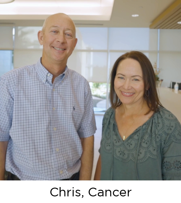 A man and woman, both white, stand in the lobby of a hospital and smile at the camera.