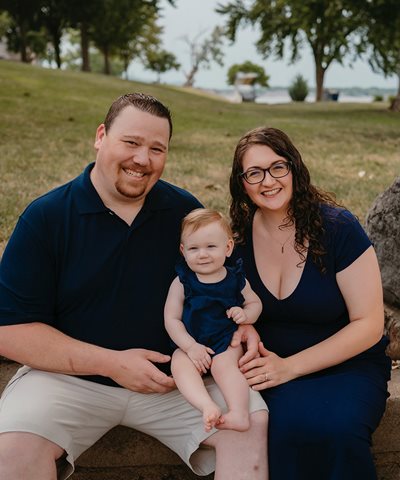 A white father, mother and toddler pose in park.